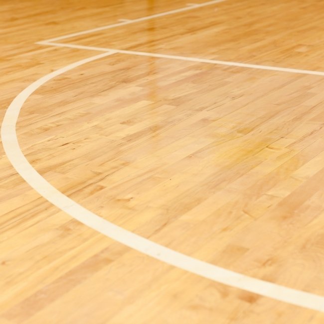 Image depicts a close up of a basketball court made with gymnasium maple hardwood floors..