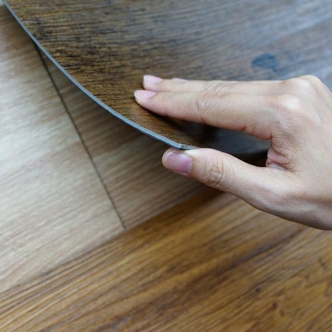 Image depicts a hand laying down a vinyl floor sheet.